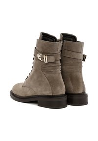 Bottes ankle en daim gris avec un bout rond, un devant à lacets, une fermeture éclair sur le côté, un détail de boucles superposées et une semelle épaisse noire.