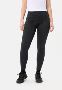 Leggings nere con un alto punto vita, design aderente e tasche laterali. Indossati con scarpe da ginnastica nere e una maglietta bianca. Tessuto elastico.