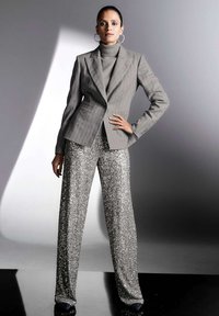 Gray pinstriped blazer over a gray turtleneck, paired with wide-leg glittery silver pants. Model stands confidently against a light backdrop.