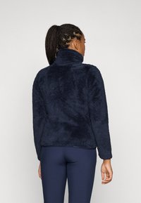 Marinblå, fluffig fleece-pullover med hög krage och långa ärmar. Tyget verkar mjukt och strukturerat, lämpligt för värme.