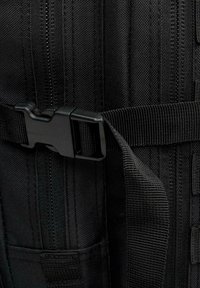 Svart tygryggsäck med spänne, släta dragkedjor och vävd textur med flera vertikala sömmar.