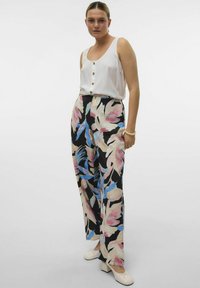 Witte tanktop met knopen, gecombineerd met zwarte bloemenbroek met grote roze en blauwe bloemen, een gladde textuur en een wijduitlopende pasvorm.
