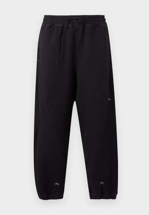 Schwarze Jogginghose mit elastischem Bund und Bündchen, schlanke Passform, dezente Nähte und kleines weißes Logo in der Nähe der Knöchel und am Oberschenkel.