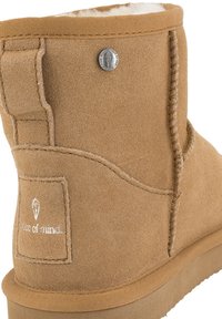 Stivale in suede beige per l'inverno con rivestimento in pile bianco e patch con logo sul tallone, caratterizzato da dettagli cuciti e un rivetto metallico vicino al bordo superiore.