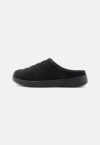 Melna zamšādas slip-on kurpe ar mīkstu augšdaļu, kas apvieno teksturētu šūtu dizainu, noapaļotu purngalu un elastīgu gumijas zoli.