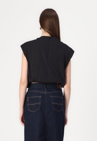 Top nero senza maniche con spalle strutturate, presenta una zip sul retro, abbinato a una gonna di jeans blu scuro con cuciture arancioni e due tasche posteriori.