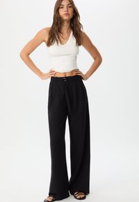 Pantaloni ampi neri con design plissettato, cintura in tessuto e zip frontale. Abbinati a un top a canotta bianco aderente, che mette in risalto la vita.