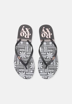 Chanclas blancas y negras con estampados florales y geométricos, con correas negras y el logo "ROXY" en la plantilla y las correas.