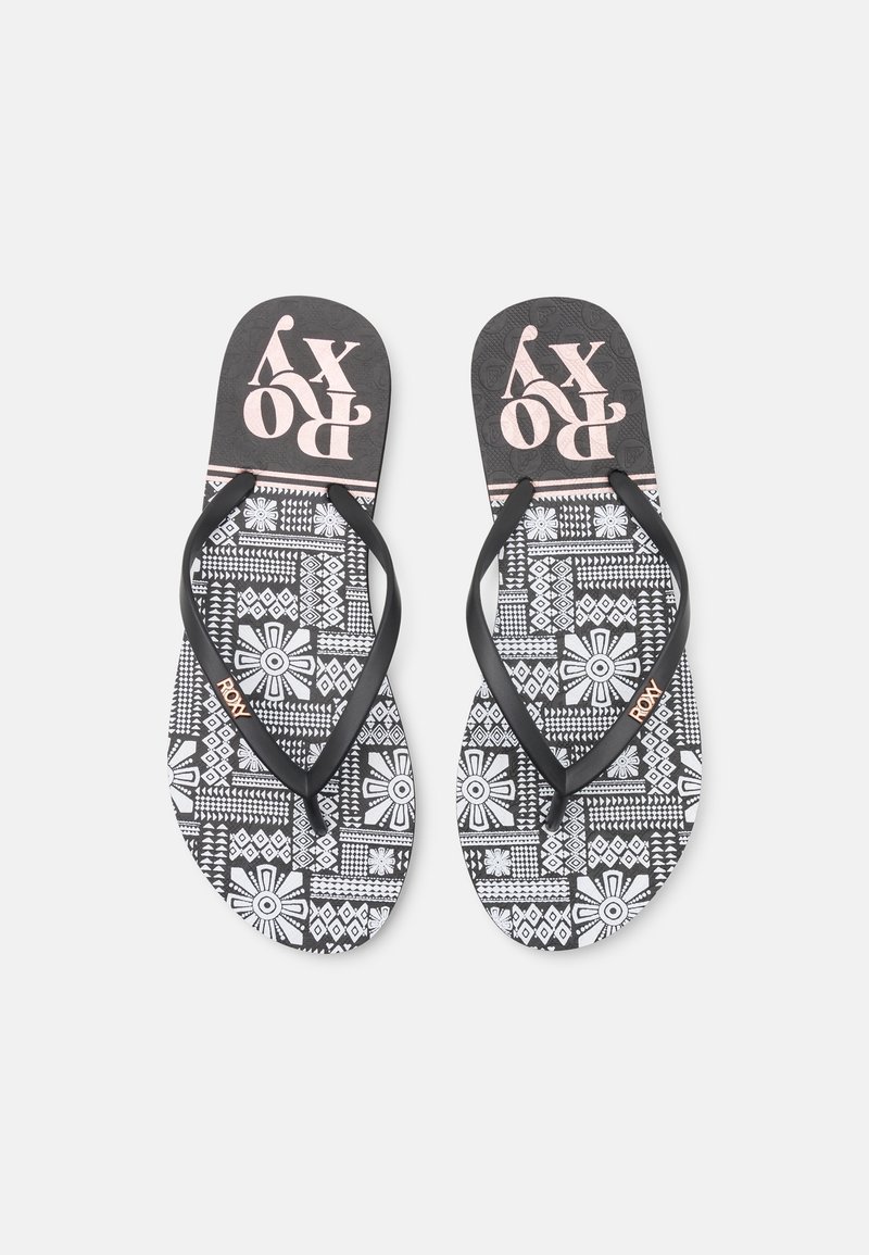 Tongs à motifs noir et blanc avec des designs floraux et géométriques, équipées de brides noires et du logo "ROXY" sur la semelle intérieure et les brides.