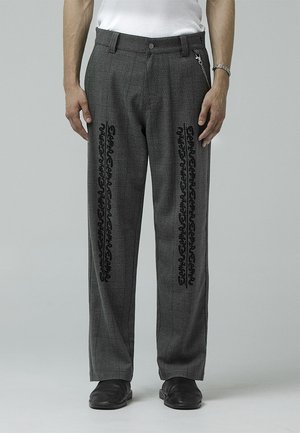 Gray plaid trousers with black decorative patterns along the sides, featuring a button closure and chain accent. Material is textured.