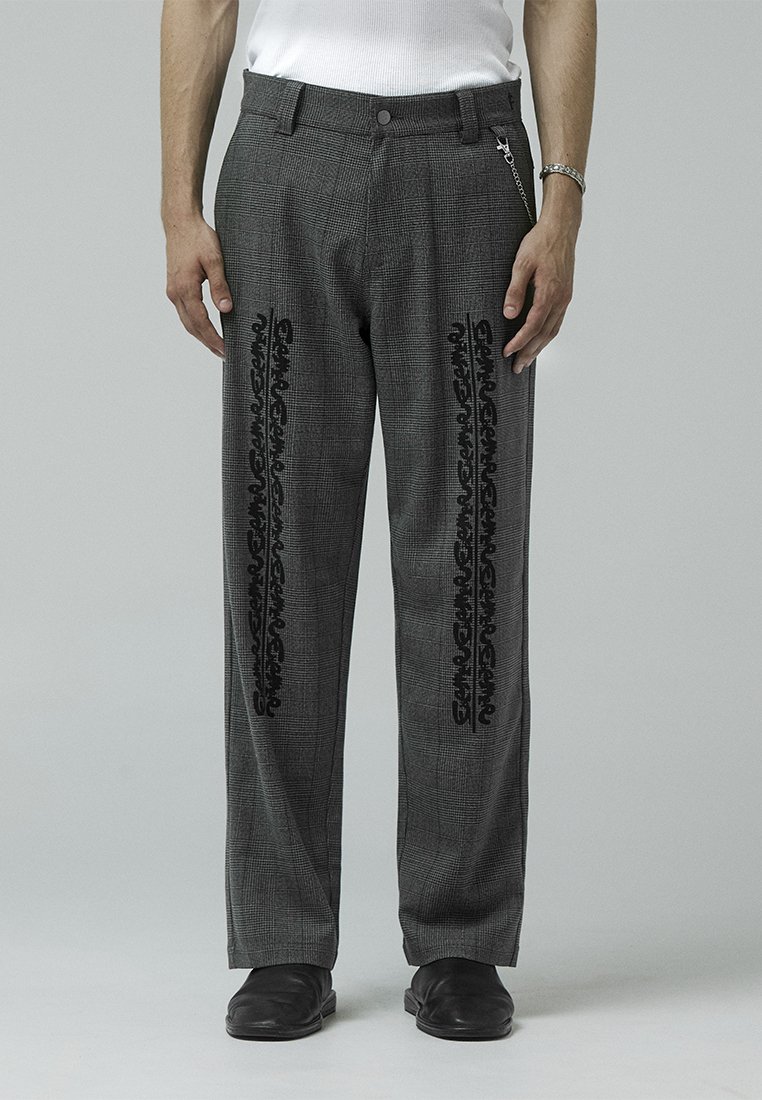 Gray plaid trousers with black decorative patterns along the sides, featuring a button closure and chain accent. Material is textured.