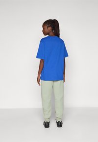 En blå oversized t-skjorte med rund hals, kombinert med lysegrønne joggebukser og svarte sko. Stoffet ser mykt ut med en avslappet passform.