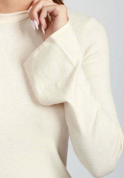 Maglione a maniche lunghe di colore crema con una texture morbida, maniche ampie e un semplice scollo rotondo. Il materiale sembra leggero e traspirante.