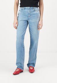 Gai zili džinsi ar taisnu kāju griezumu, kam ir augsta jostasvieta un neliela nolietojuma forma. Apvienoti ar sarkaniem plakanām kurpēm.