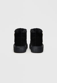 Botas de tornozelo em camurça preta apresentam um forro de pelúcia sintética, uma sola de borracha texturizada e um pequeno detalhe decorativo na lateral.
