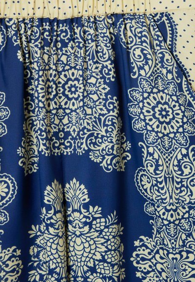 Tessuto blu navy con motivi floreali e paisley beige, caratterizzato da una vita arricciata e dettagli a pois nella parte superiore.