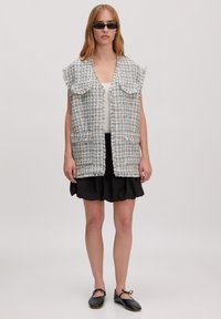 Grijze tweed vest met rafelranden, voorflapzakken en open ontwerp. Draag het over een witte top en combineer het met een zwarte skaterrok.
