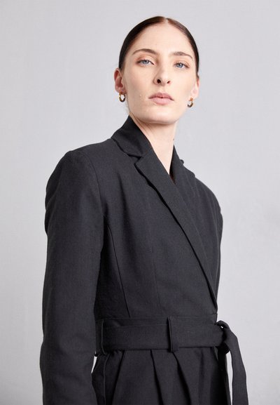 Rochie neagră, dintr-un material texturat. Dispune de un guler decupat, mâneci lungi și o curea din același material la talie, creând o siluetă ajustată.