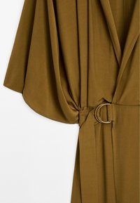 Abito avvolgente verde oliva con maniche ampie, cintura con un anello in metallo dorato e una texture di tessuto liscia.