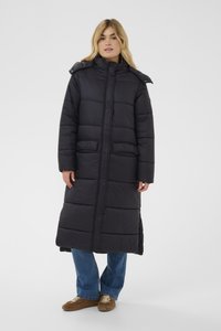 Garš melns pūkains mētelis ar kapuci, priekšā rāvējslēdzējs, divas priekšējās kabatas un pāršūts raksts. Gluda tekstūra un brīvs piegriezums.