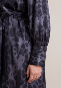 Vestito camicia in satin viola scuro con stampa leopardata. Presenta una vita cinchata, maniche lunghe a sbuffo e dettagli con polsini abbottonati.