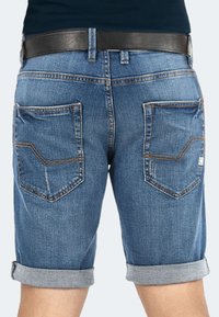 Denim shorts in blue, featuring roll-up cuffs, two back pockets with stitched accents, and a smooth black leather belt.
