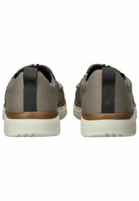 Zapatillas de tela gris con parte superior texturizada, acentos en el talón marrón contrastante y una suela de goma blanca. Presentan una etiqueta negra en el talón.