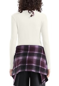 Biały prążkowany top z długim rękawem w połączeniu z czarno-fioletową flanelową koszulą w kratę, zawiązaną w talii, o zaokrąglonym spodzie i miękkiej fakturze.