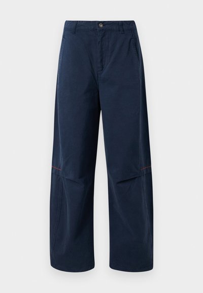 Tamsiai mėlynos plačios kelnės su priekiniais mygtukais, diržo kilpelėmis, šoniniais kišenėmis ir subtilia raudona siūle virš kelio.