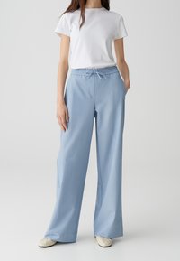 Light blue, wide-leg trousers with a drawstring waistband and side pockets, made of a smooth fabric with a subtle texture.
