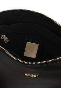 Interno di una borsa in pelle nera con zip dorata, tasca con zip e hardware dorato; presenta una texture liscia e una placca con logo.