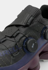 Black athletic shoe featuring a textured upper, BOA lacing system, purple midsole, and contrasting yellow stitching details.