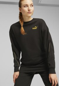 Musta puuvillane sweatshirt, millel on pehmed materjalid ja pikad varrukad, millel on kuldne Puma logo ja aktsentõmblused varrukate ääres.