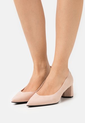 Escarpins en daim rose blush avec un bout pointu et un talon haut épais. Présentent une finition lisse et un léger design découpé sur le cou-de-pied.