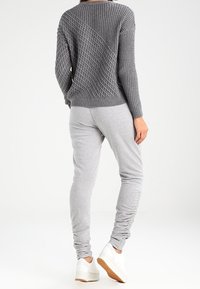 Grauer Strickpullover mit strukturiertem Muster; kombiniert mit hellgrauen, schmal zulaufenden Jogginghosen und weißen Turnschuhen mit hellbrauner Sohle.