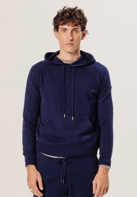 Hoodie bleu marine en tissu doux, doté d'une poche frontale, d'une capuche avec cordons de serrage, et de poignets et d'un ourlet côtelés. Surface lisse et texturée.