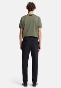 Grünes Baumwoll-T-Shirt mit kurzen Ärmeln, kombiniert mit schwarzen Hosen mit elastischem Bund und zwei Gesäßtaschen. Einfaches und vielseitiges Design.