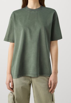 T-shirt met korte mouwen en ronde hals, gemaakt van olijfgroen katoen. Comfortabele pasvorm, zachte textuur, zichtbare stiksels langs de halslijn en zoom.