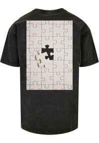 Sort kortærmet t-shirt med et stort hvidt puslespils grafik på bagsiden, med to mismatchede puslespilsbrikker i sort og hvid.