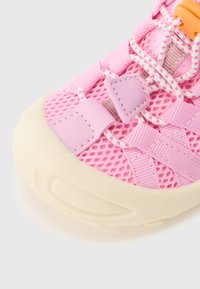 Ροζ αθλητικό παπούτσι από δίχτυ με ροζ και λευκά κορδόνια, ραμμένα δερμάτινα κομμάτια και παχιά λαστιχένια σόλα εκρού, ορατή σε κοντινή λήψη.