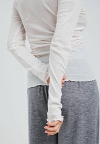 Langärmliges, hellgraues Oberteil aus weichem, transparentem Stoff, mit Rundhalsausschnitt und gewelltem Saum, kombiniert mit dunkelgrauen, weichen Hosen.