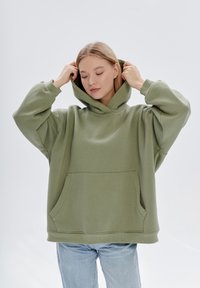 Felpa verde oliva realizzata in tessuto morbido, con una grande tasca frontale, vestibilità ampia e cappuccio con cordoncino regolabile per maggiore comfort.