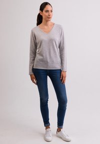Maglione grigio chiaro a maniche lunghe con scollo a V realizzato in materiale morbido, abbinato a jeans slim-fit blu e sneakers bianche. Design semplice senza motivi.