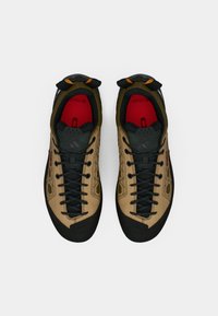 Παπούτσια αναρρίχησης σε απόχρωση ταμπά και ελιάς με υφασμάτινο επάνω μέρος, αντιθετική μαύρη λαστιχένια σόλα και μαύρα κορδόνια· εσωτερική επένδυση σε κόκκινο χρώμα.