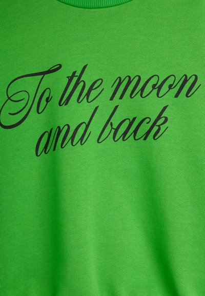 Πράσινο ένδυμα με μαύρο χειρόγραφο κείμενο που αναγράφει «Στο φεγγάρι και πίσω» τυπωμένο μπροστά.