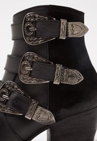 Černá kotníková bota vyrobená z kůže a semiše, s třemi dekorativními stříbrnými sponami. Disponuje texturovaným povrchem a patou s vrstvami.