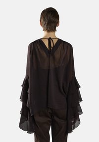 Czarna, prześwitująca bluzka z warstwowymi falbanami na rękawach, dekoltem w kształcie litery V z tyłu i zawiązywaniem. Miękka tkanina o zwiewnym kroju i teksturowanych detalach.