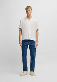Witte linnen shirt met korte mouwen en een knopen front, gecombineerd met donkerblauwe denim jeans en crème sneakers. Eenvoudig design, relaxed fit.