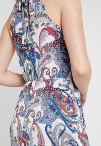 Gros plan d'une robe sans manches avec un motif cachemire multicolore en rouge, bleu et blanc, portée par une personne montrant son dos et son bras.
