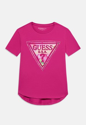 Ryškiai rožinė trumpomis rankovėmis marškinėliai su gėlių raštų trikampiu logotipu, kuriame parašyta "GUESS U.S.A." ir centre yra klaustukas.